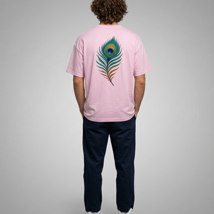 Person wearing a pink t-shirt with a peacock feather design on the back, standing against a gray background.